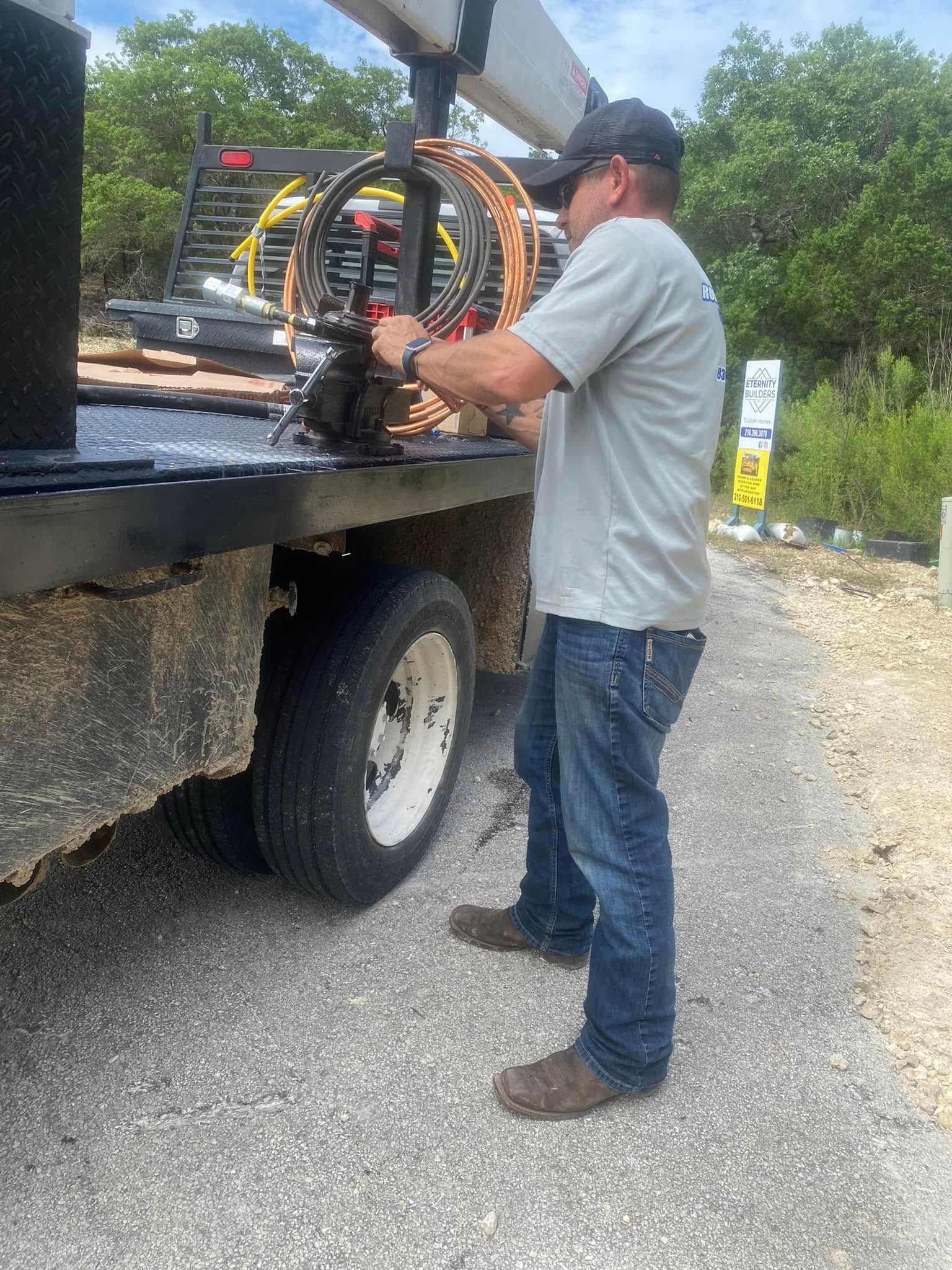 Man in a cap loading a metal machine onto a flatbed truck outdoors on gravel.