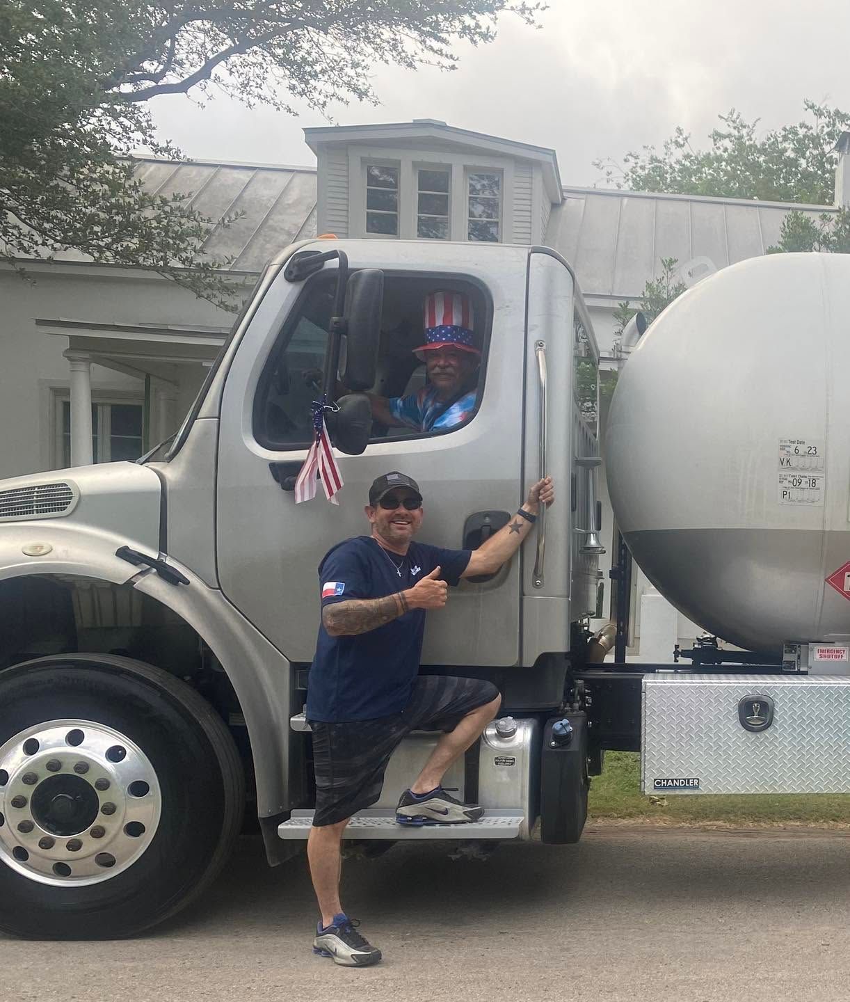 Man beside a silver tanker truck with driver in cab, parked near a building
