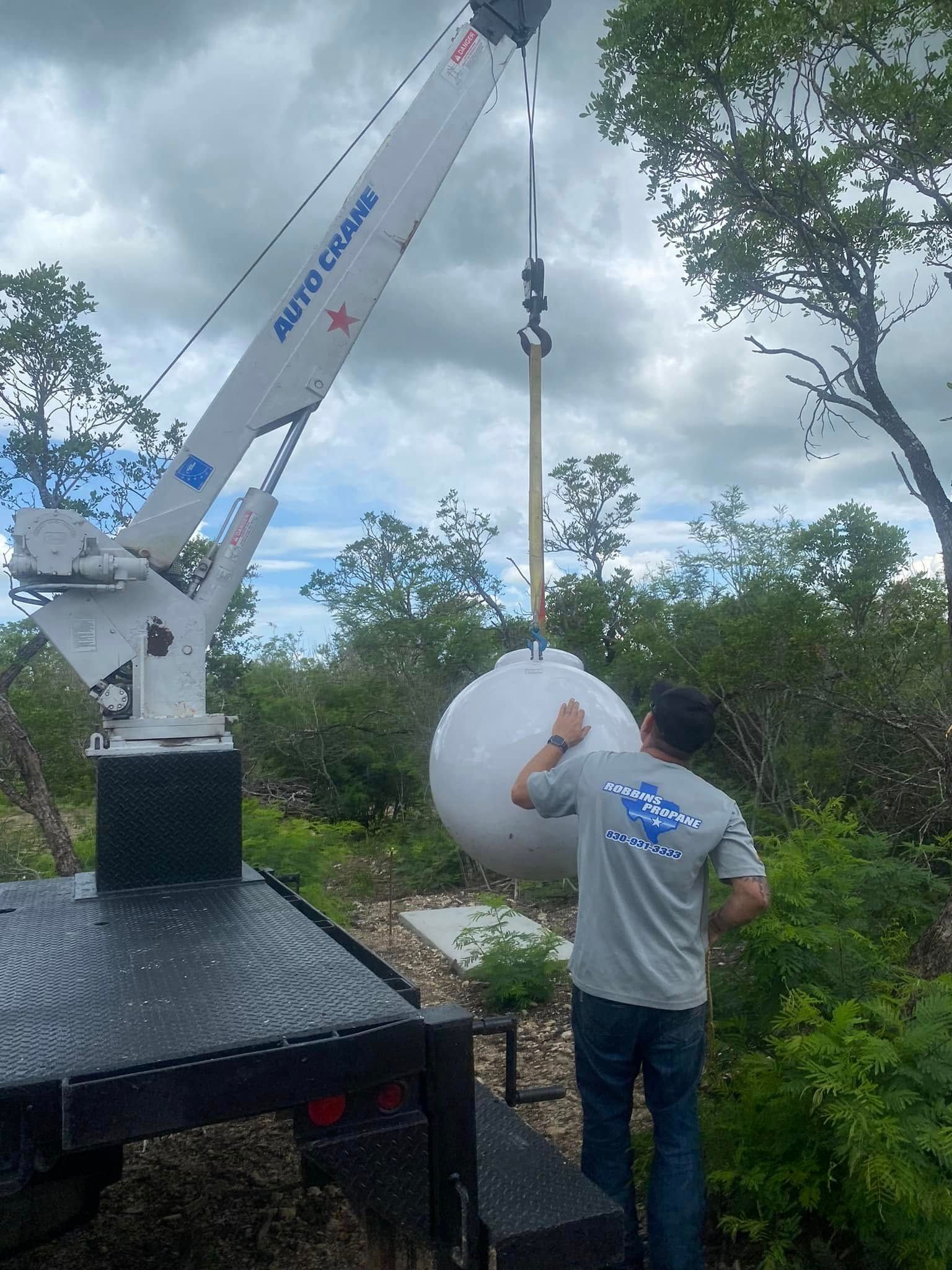 Crane lifting a large white spherical object while a worker guides it outdoors under cloudy skies
