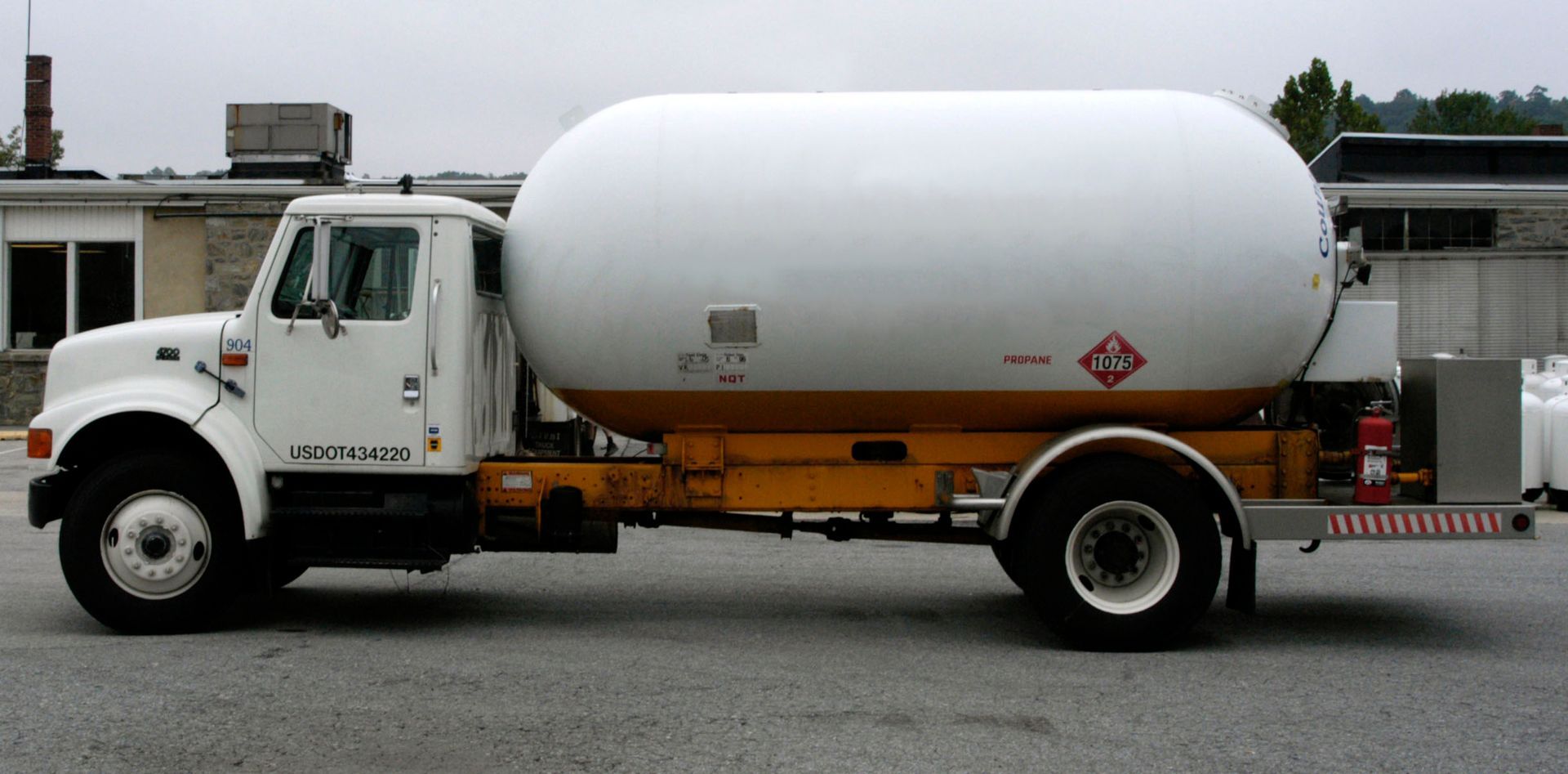 White tanker truck parked on pavement with an orange chassis and red hazard placard