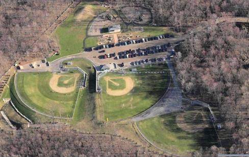 Aerial view of a public park featuring three baseball fields, a central parking lot, and surrounding wooded areas.