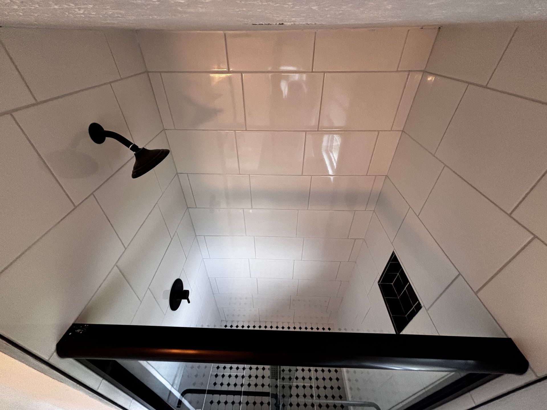 A shower with white tiles and a black shower head