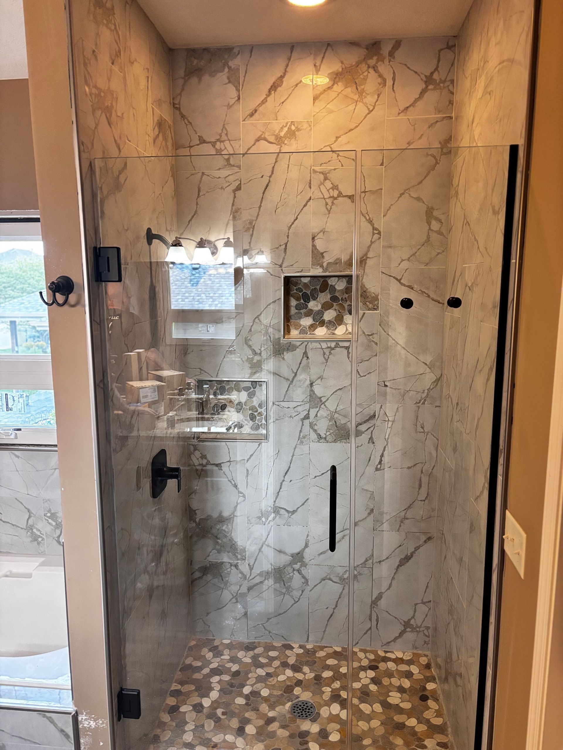 A bathroom with marble tiles and a walk in shower with a glass door.