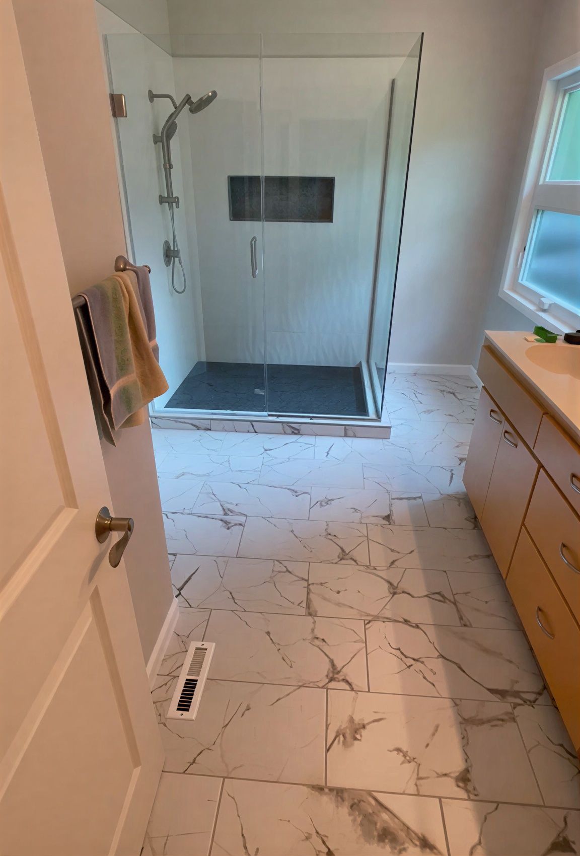 Modern bathroom with glass shower, white marble floor, and wood vanity.