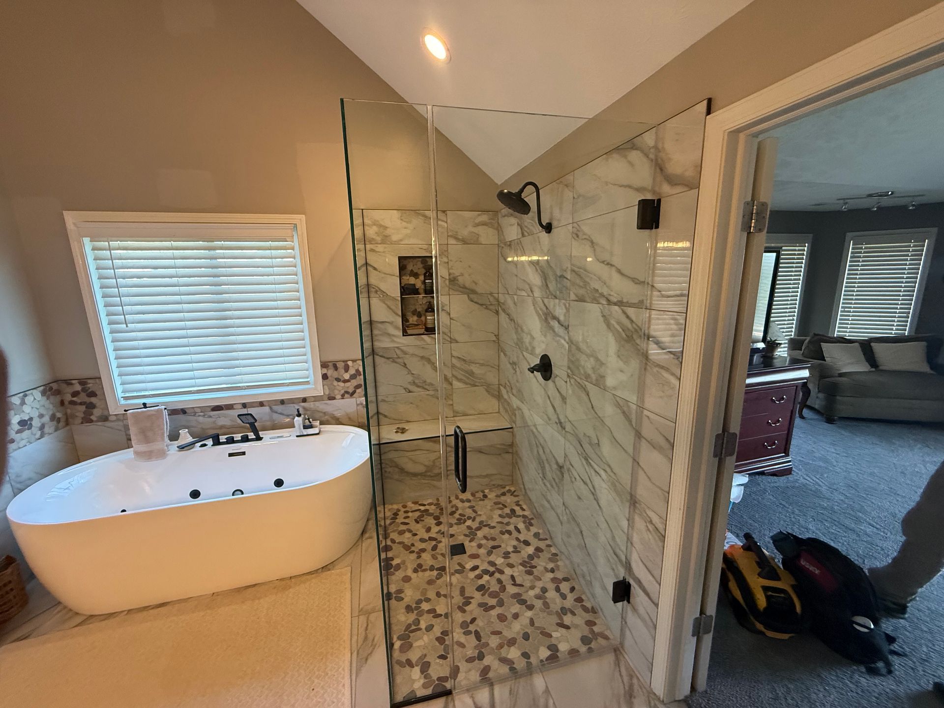 Bathroom with freestanding tub, glass shower, and marble tile, viewed through an open doorway