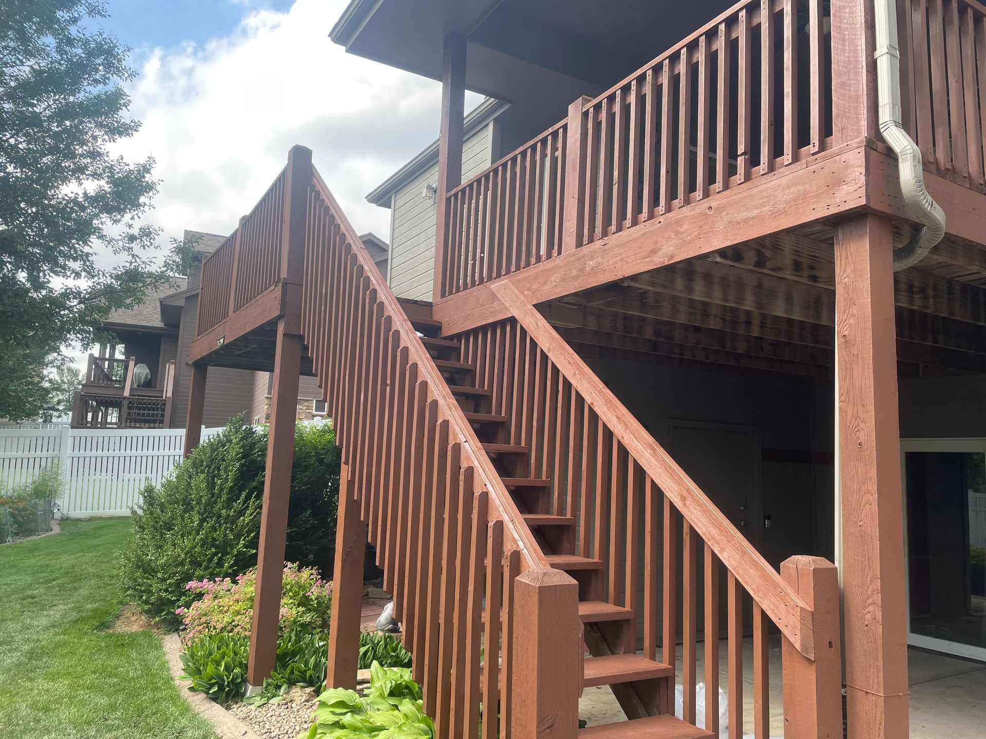 A wooden deck with stairs leading up to the second floor of a house.