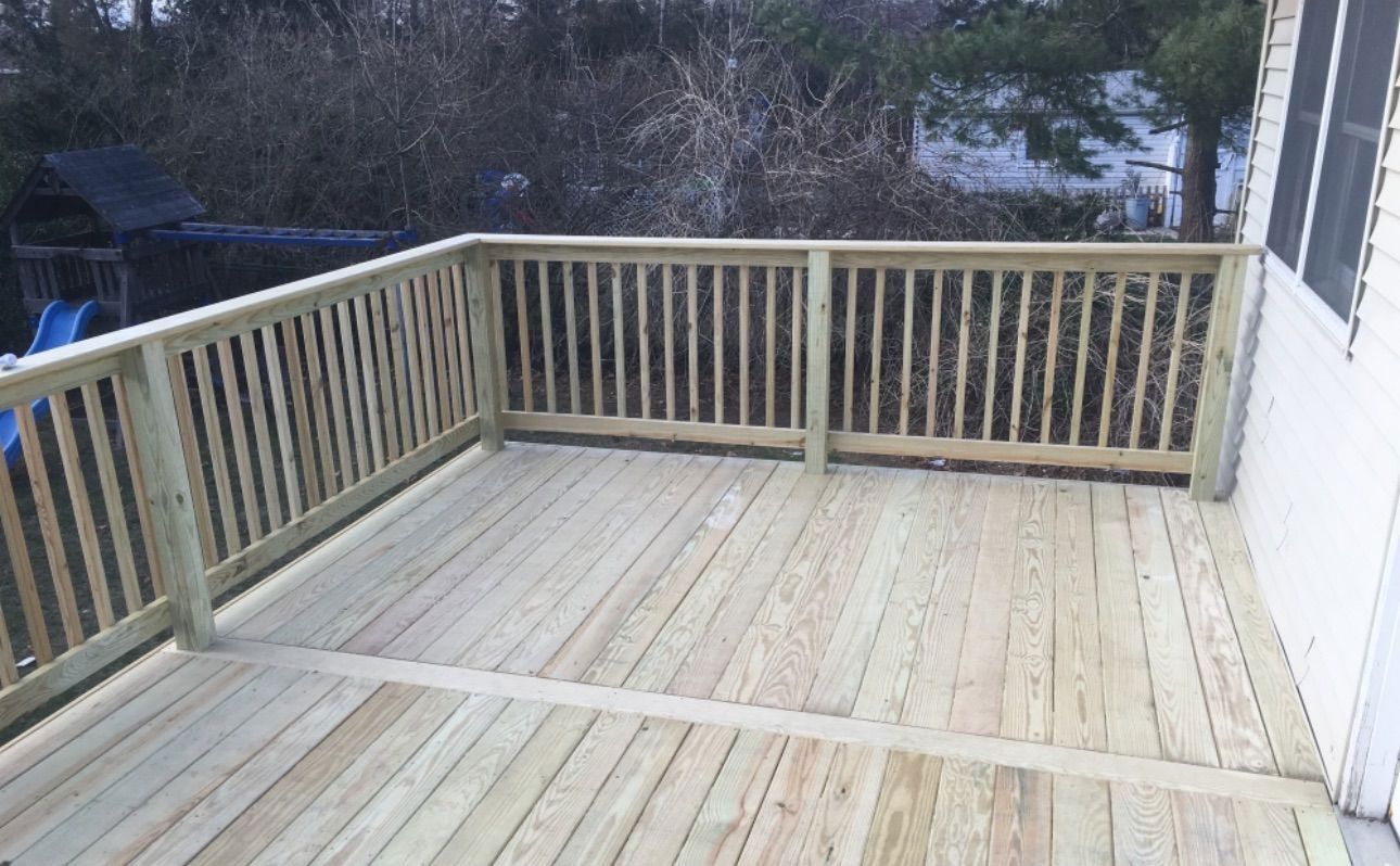 A wooden deck with a railing and a slide in the background.