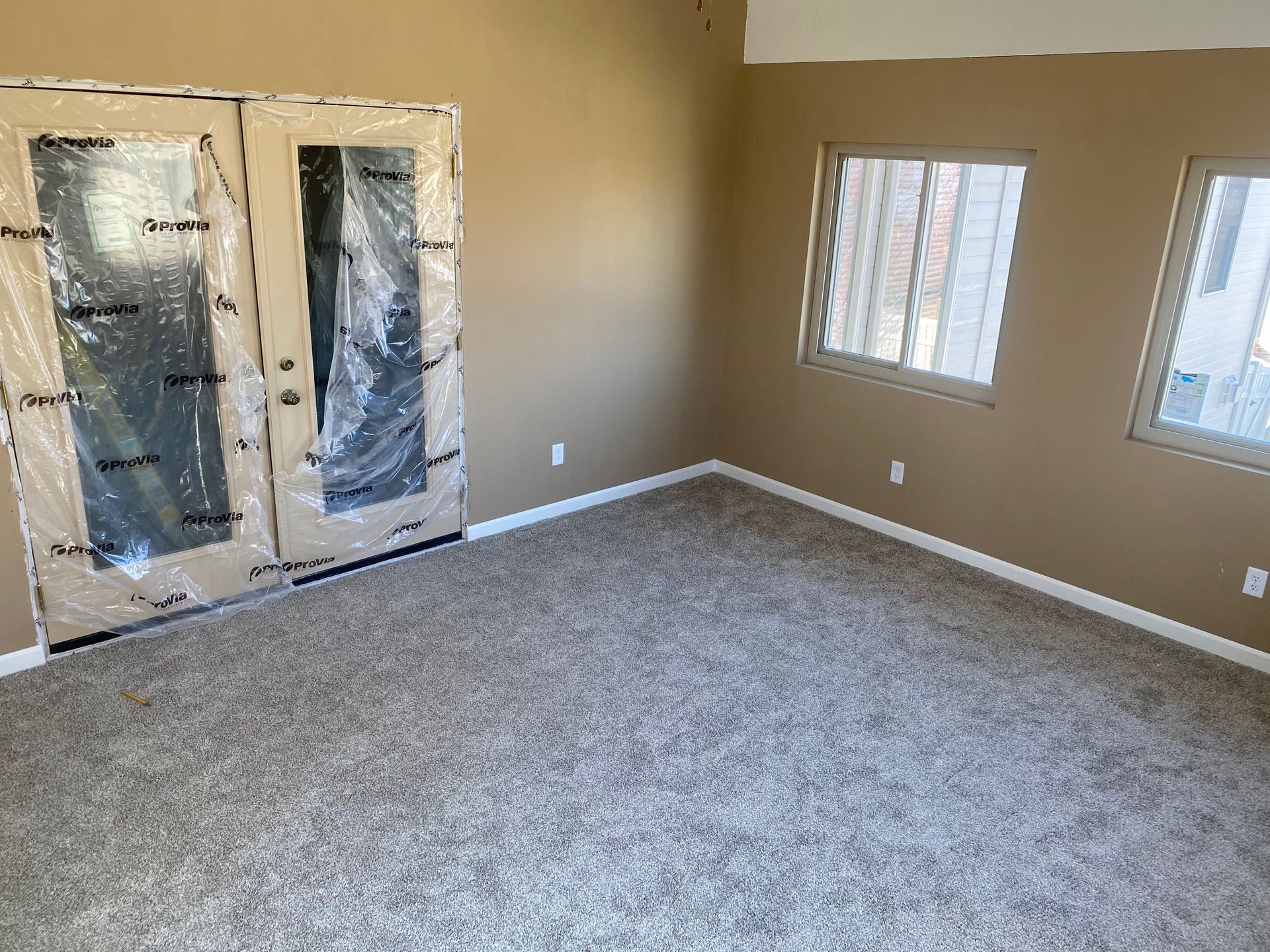 An empty room with a carpeted floor and two windows.