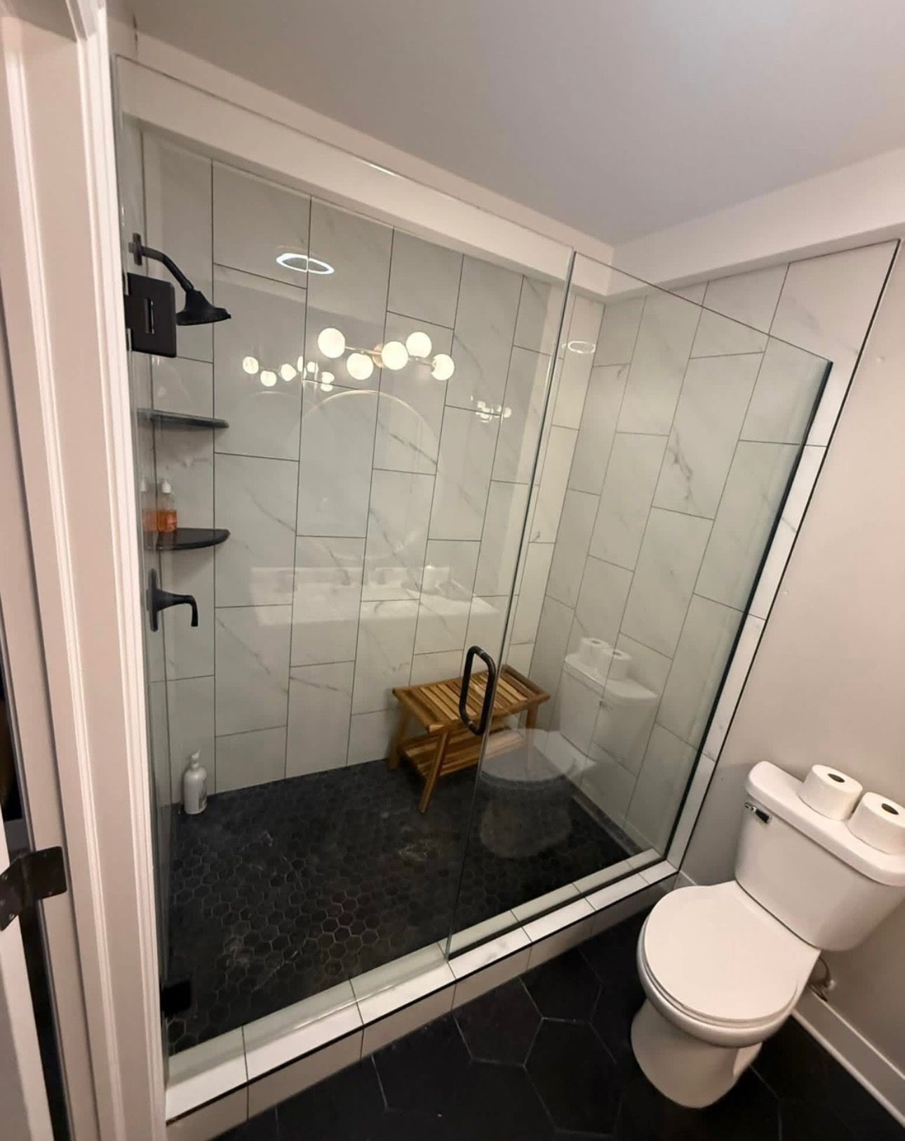 Modern bathroom with glass shower, black fixtures, and white tiled walls.
