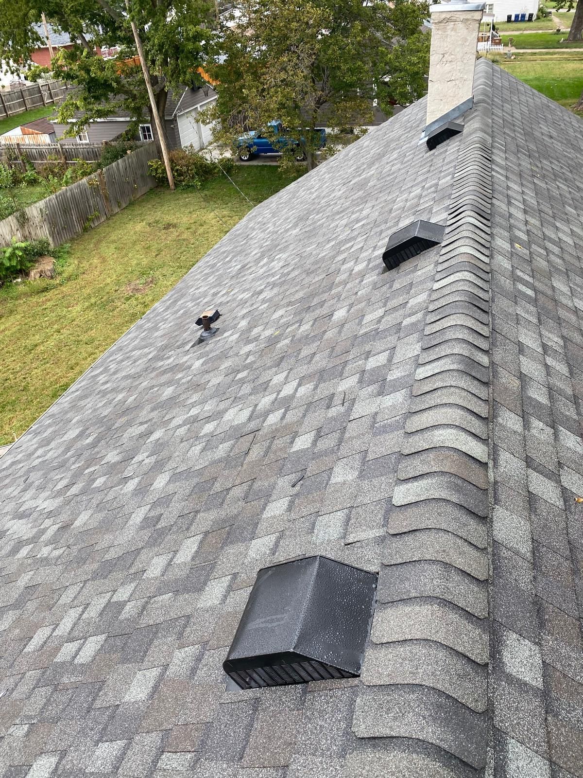 Gray shingled roof with three black vents, chimney, and grass visible in background.