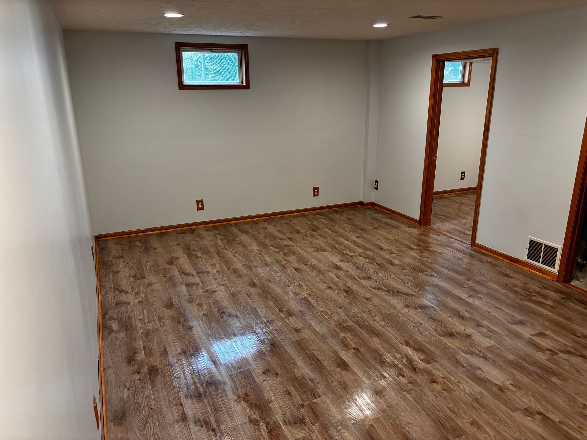 An empty basement with hardwood floors and white walls.