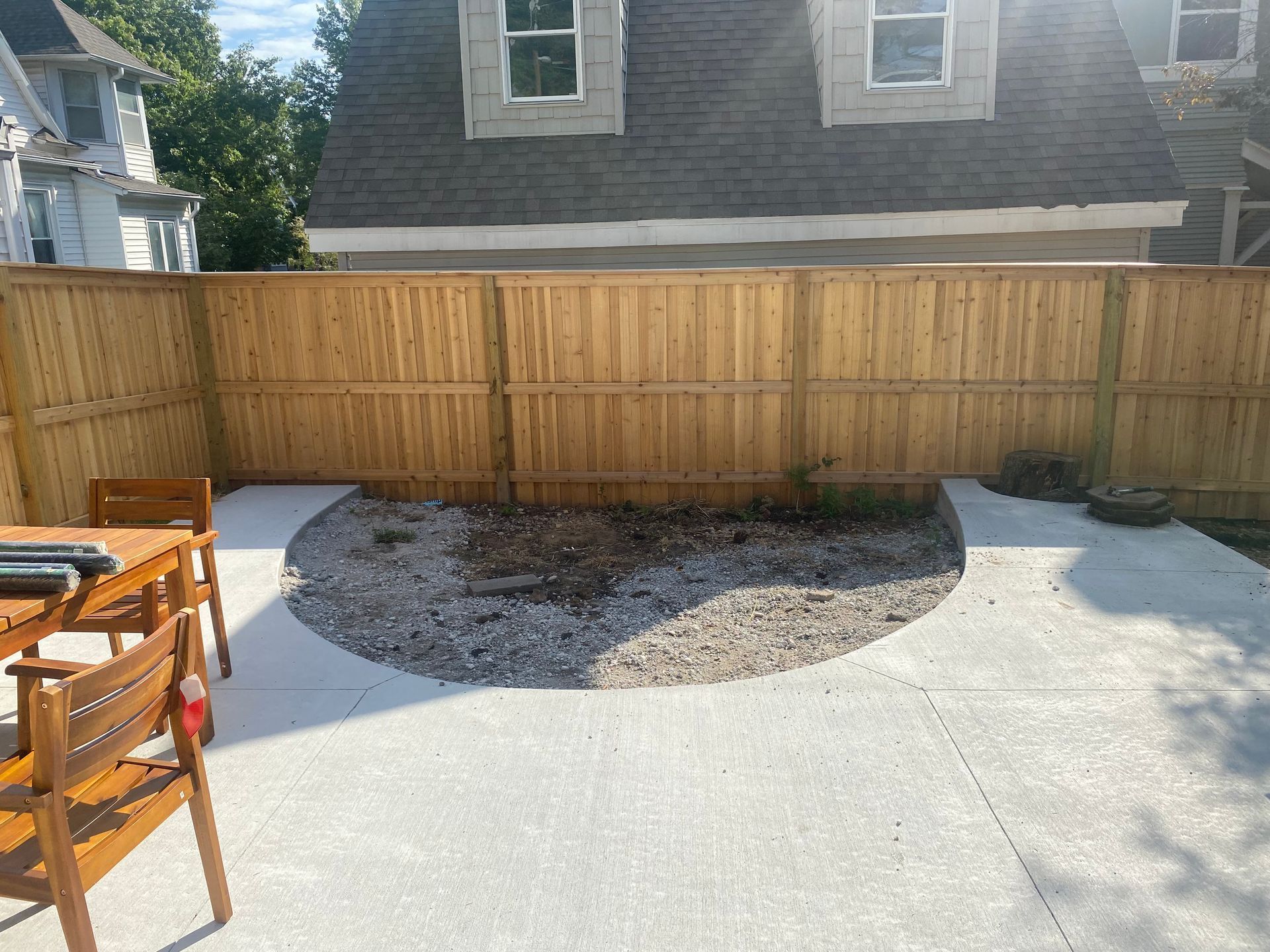 A wooden fence surrounds a patio with a table and chairs.