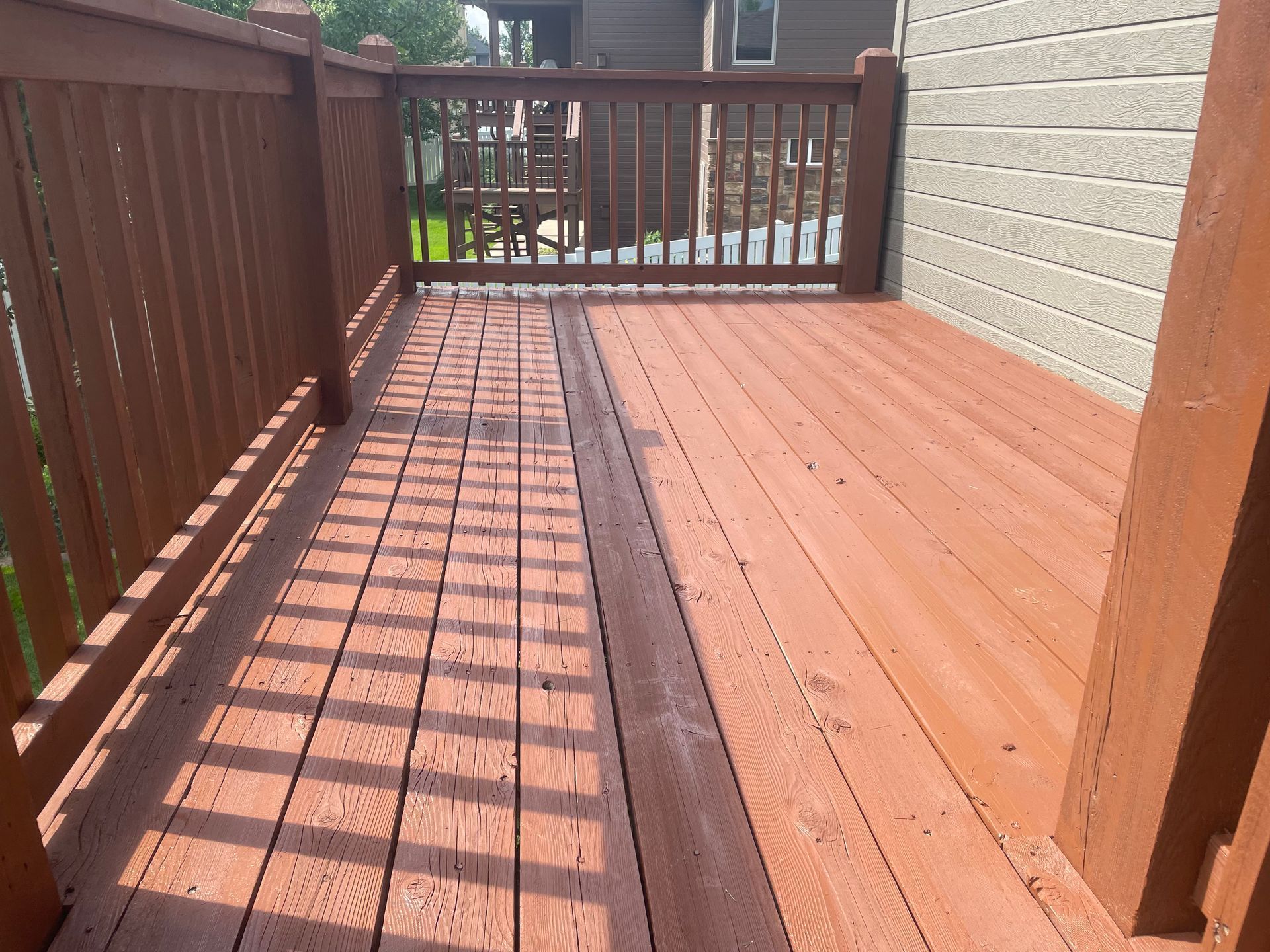 A wooden deck with a railing and a house in the background.