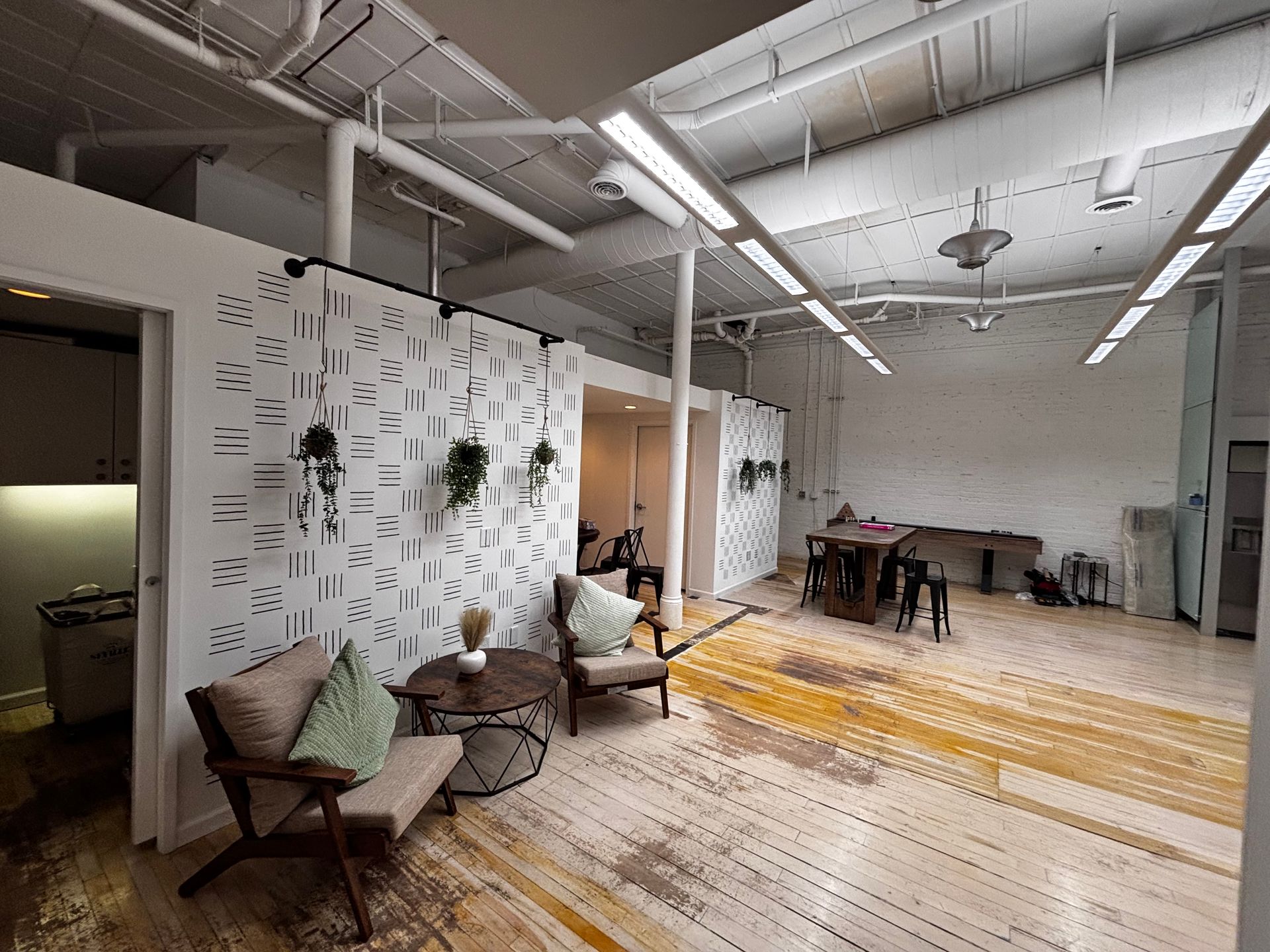 Spacious interior with white walls, exposed pipes, wooden floor, seating area, and decorative panels.