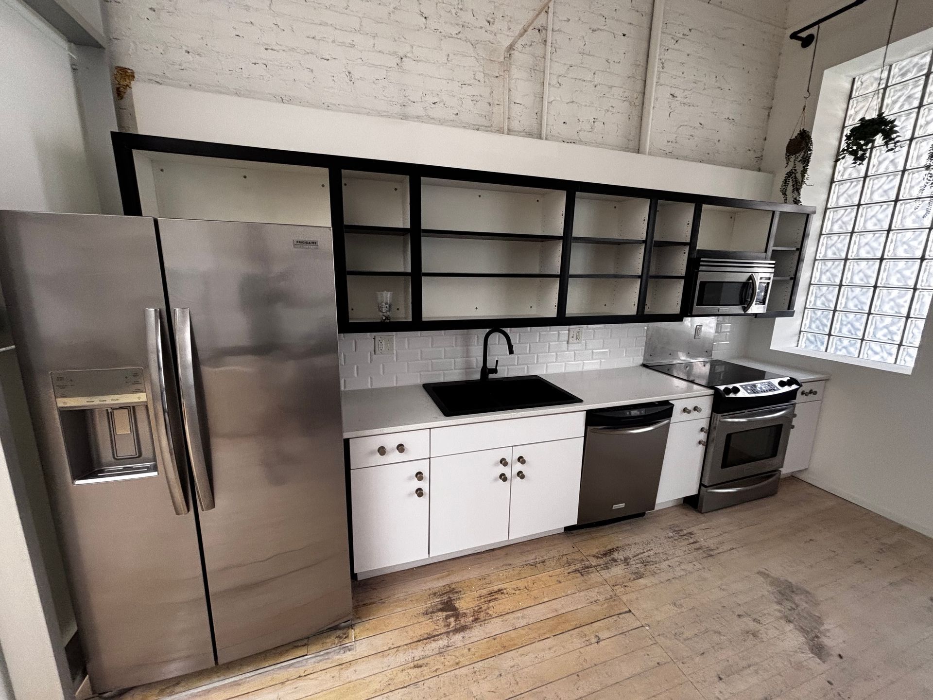 Kitchen with stainless steel appliances, white cabinets, black countertops, and open shelving.