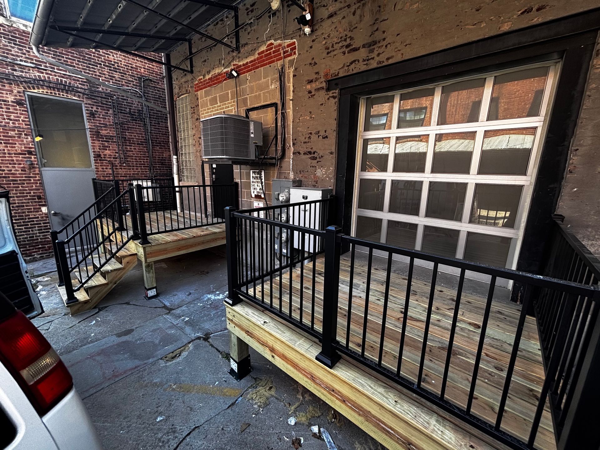 Alleyway with black railings, wooden decks, and a garage door entrance. Red brick wall.