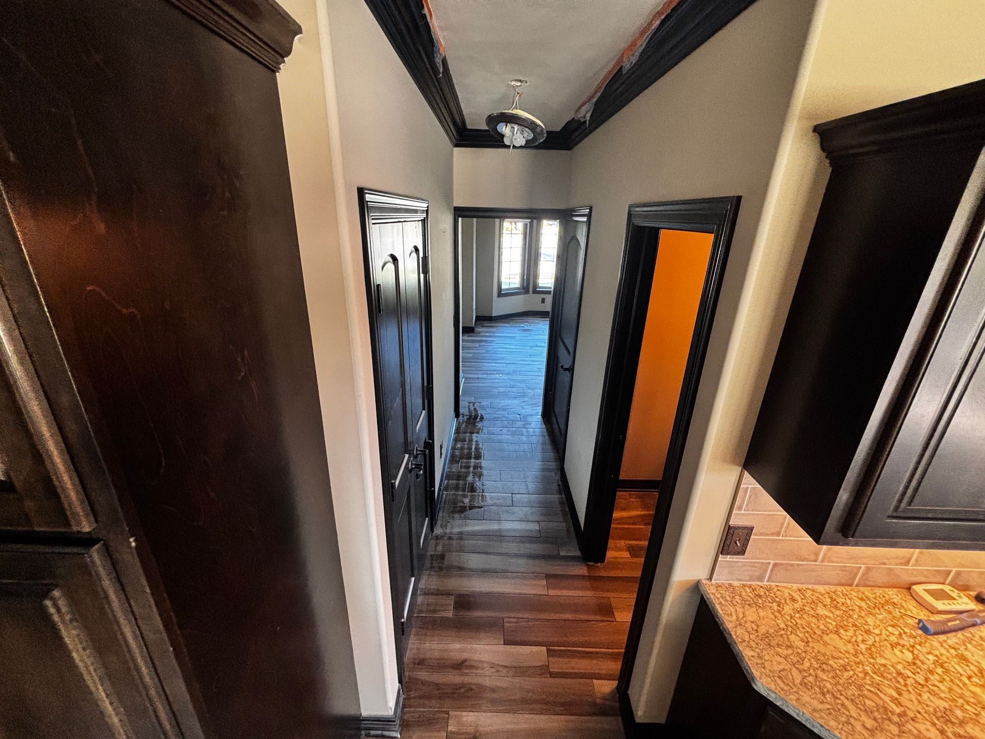 Hallway with dark cabinets and doors, leading to a room with windows.