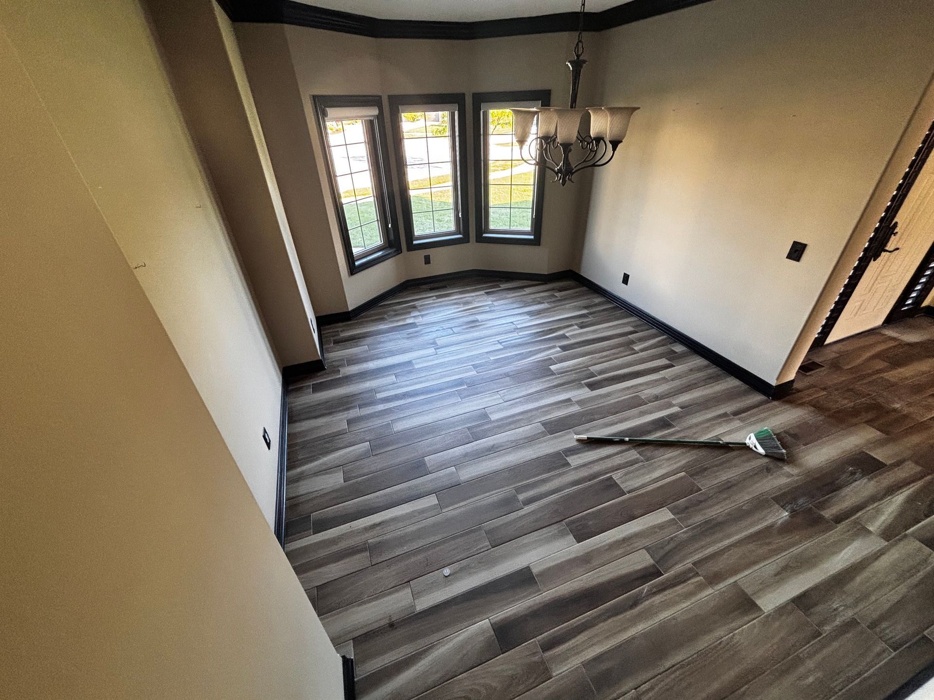 Dining room with gray wood-look flooring, large windows, and a chandelier; walls are beige.