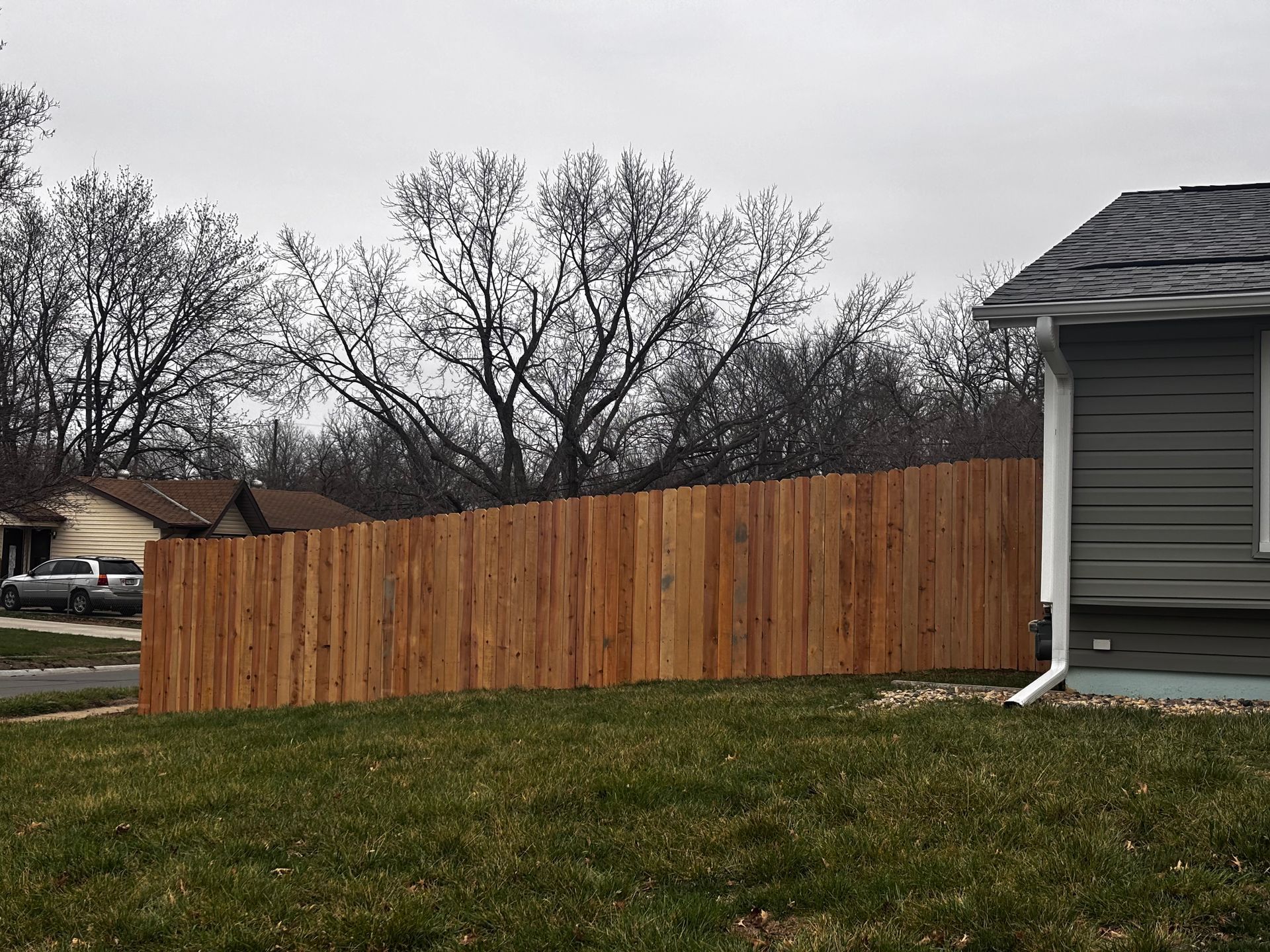 A wooden fence surrounds a house in a residential area.