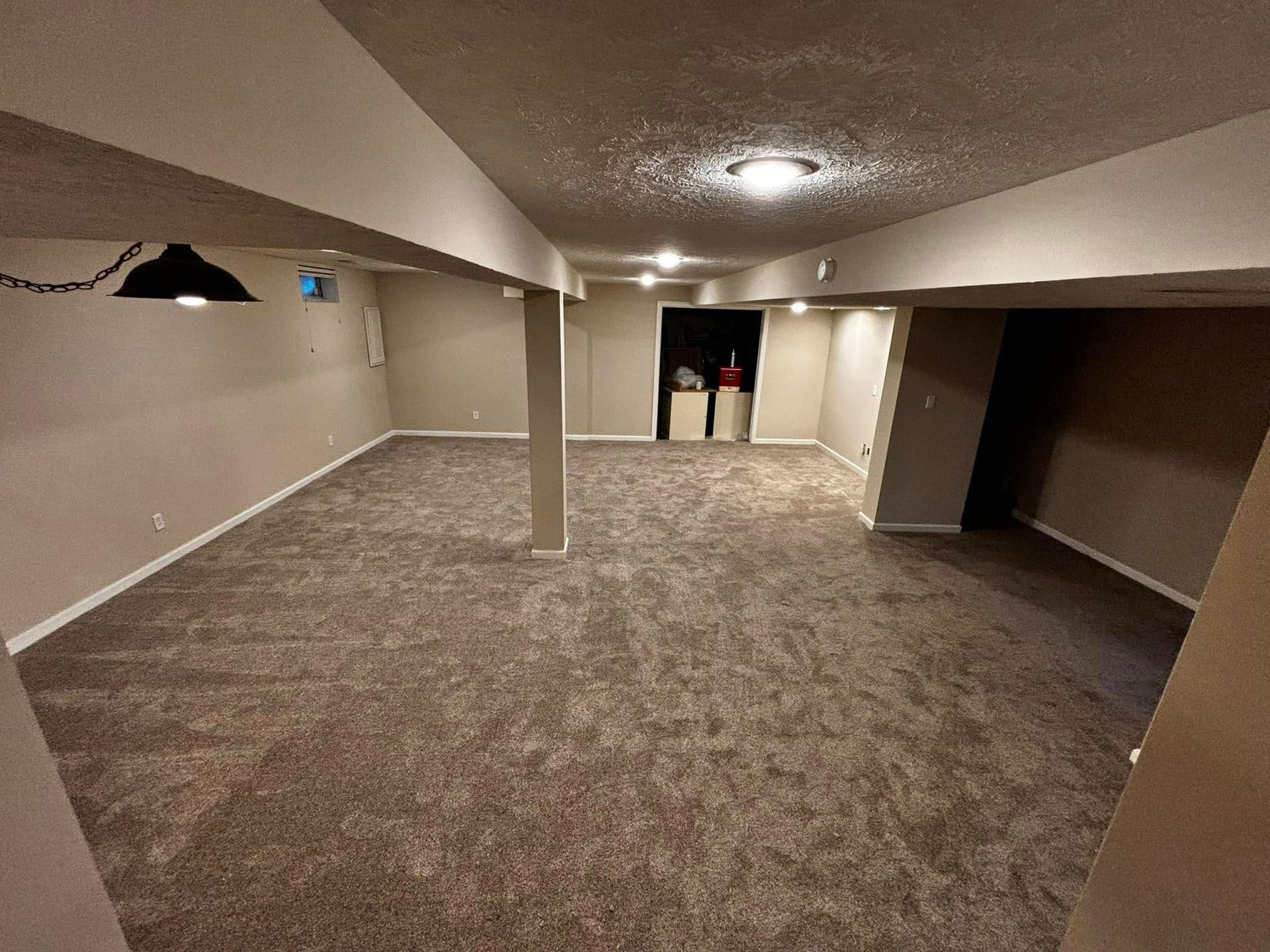 An empty basement with a carpeted floor and a pool table.