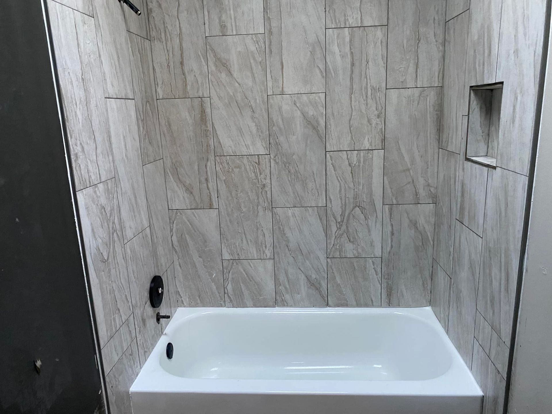 A bathtub is sitting in a bathroom next to a tiled wall.