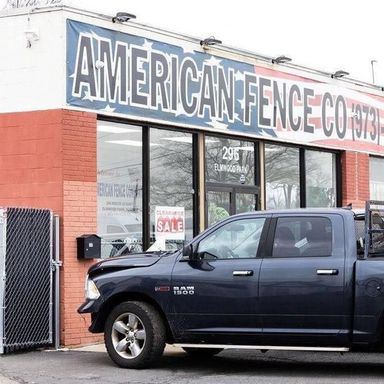 A blue pickup truck parked in front of an American Fence Co. building.