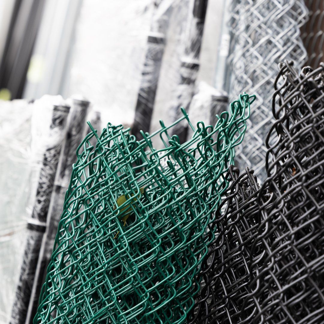 Green and black chain-link fence rolls stacked, with other fence materials in the background.