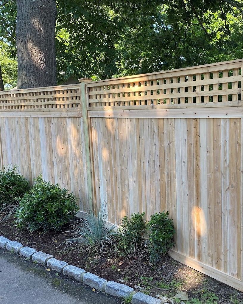 Wooden fence with lattice top, next to shrubs and a sidewalk.