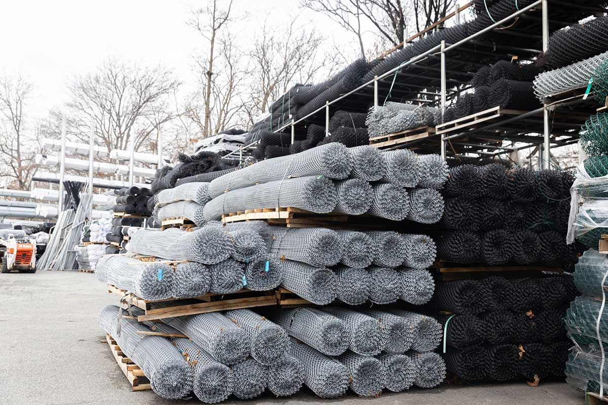 Piles of rolled chain link fencing in various colors at an outdoor storage facility.