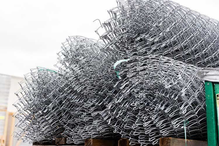 Rolled-up chain-link fence stacked on a pallet, ready for installation.