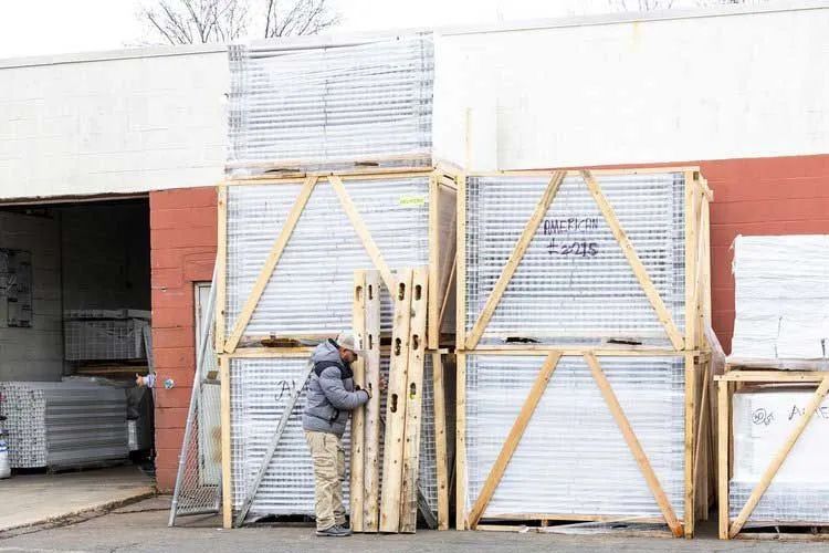 Person inspecting stacked wooden crates outside a brick building, potentially construction materials.