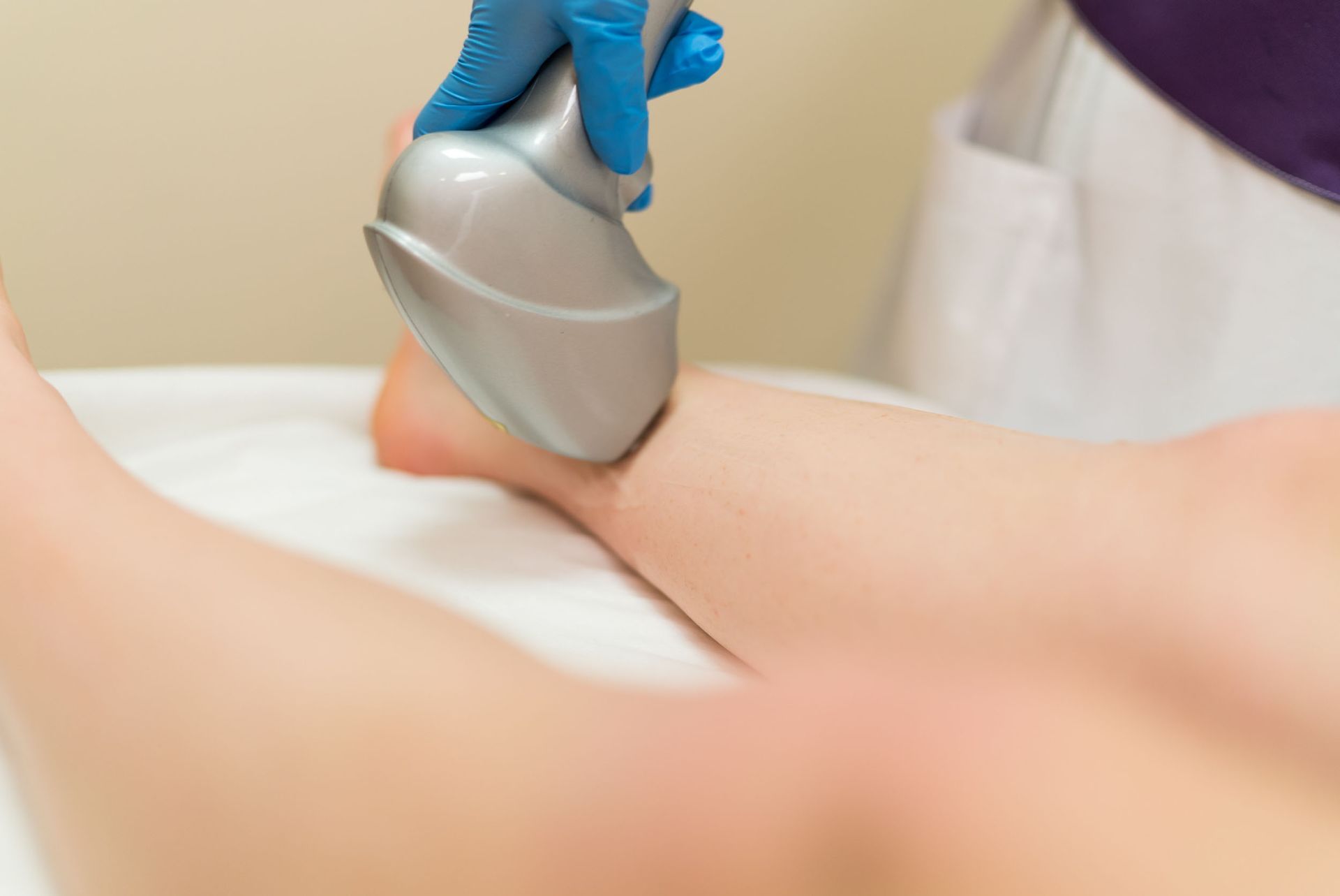 A person receiving laser hair removal on their leg; technician wearing blue glove.