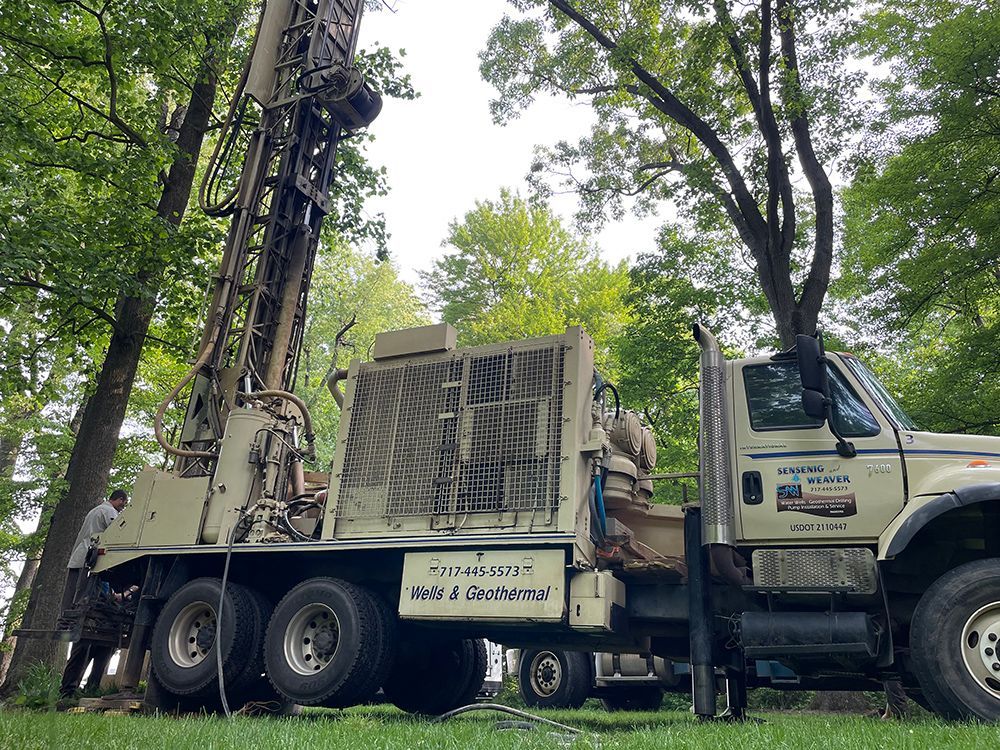 A truck with a drilling rig on the back is parked in the grass.