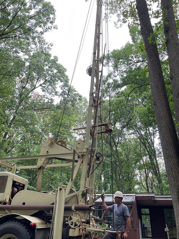 A man is standing next to a large machine in the woods.
