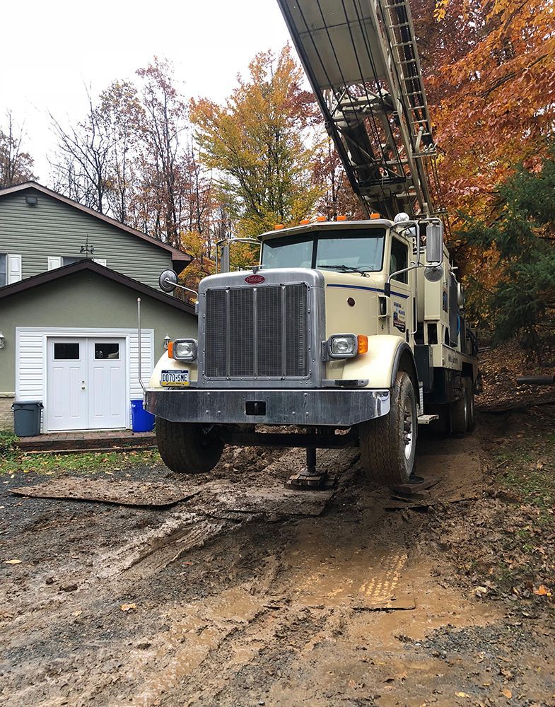 A large truck is driving down a dirt road in front of a house.