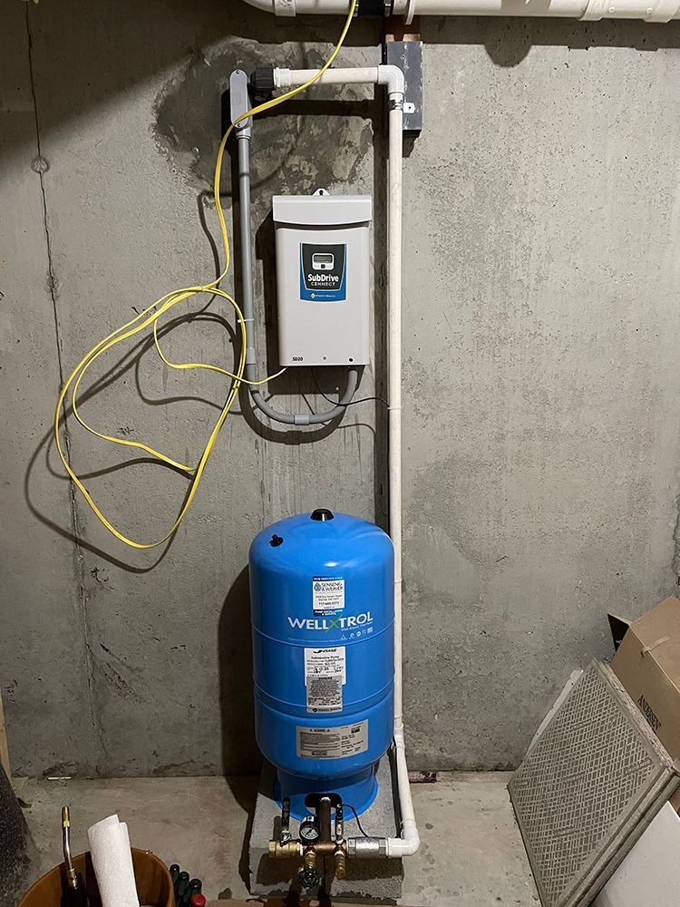 A blue water tank is sitting in a basement next to a wall.