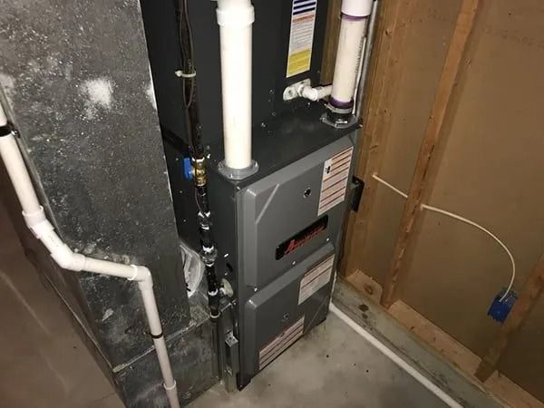 Furnace installed against a concrete wall, with white pipes and exposed framing.