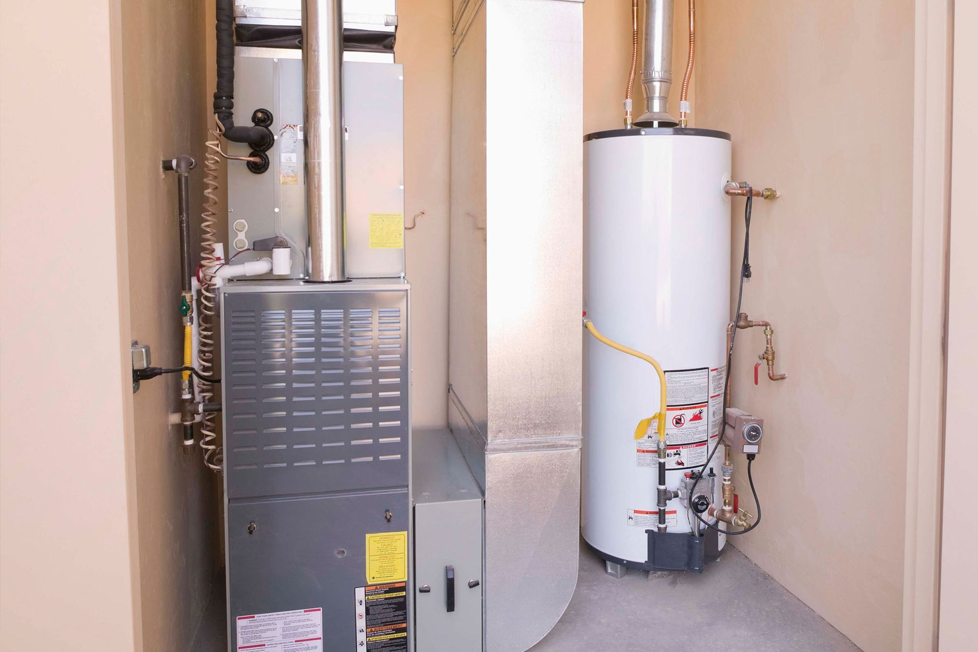 Water heater and furnace in a narrow utility closet with beige walls and gray carpet.