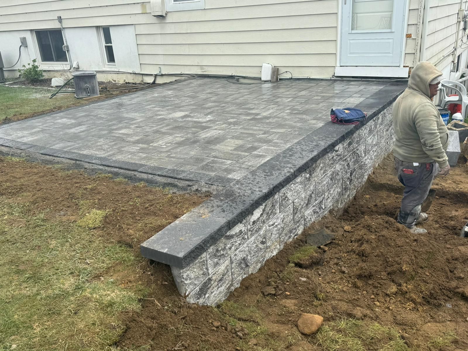 A man is working on a patio in front of a house.