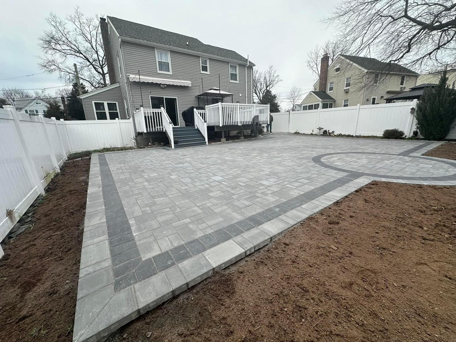 The backyard of a house with a patio and a white fence.