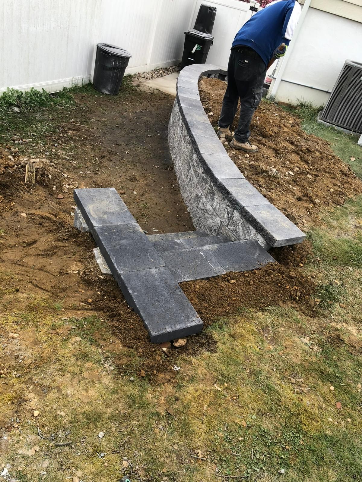 A man is working on a stone wall in a backyard.