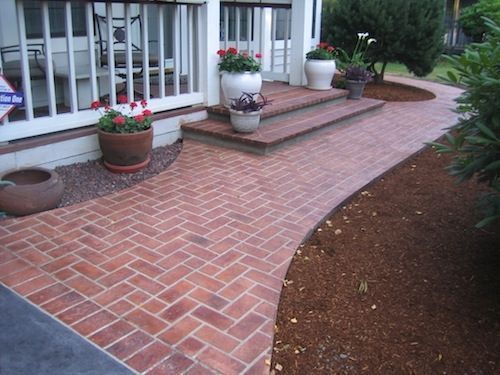 A brick walkway leading to a porch with potted plants
