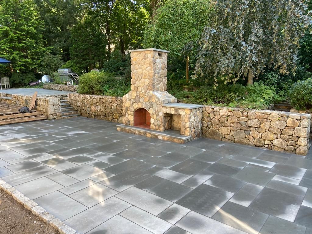 A stone fireplace is sitting on a patio next to a stone wall.