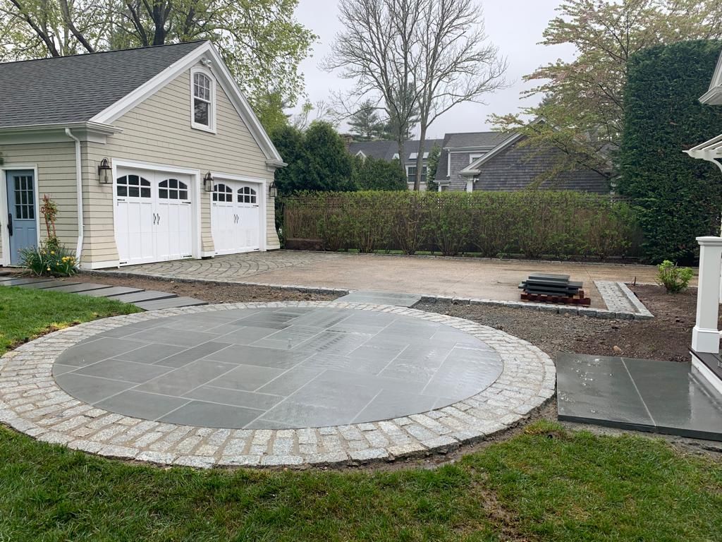 There is a circular patio in the middle of the yard in front of a garage.