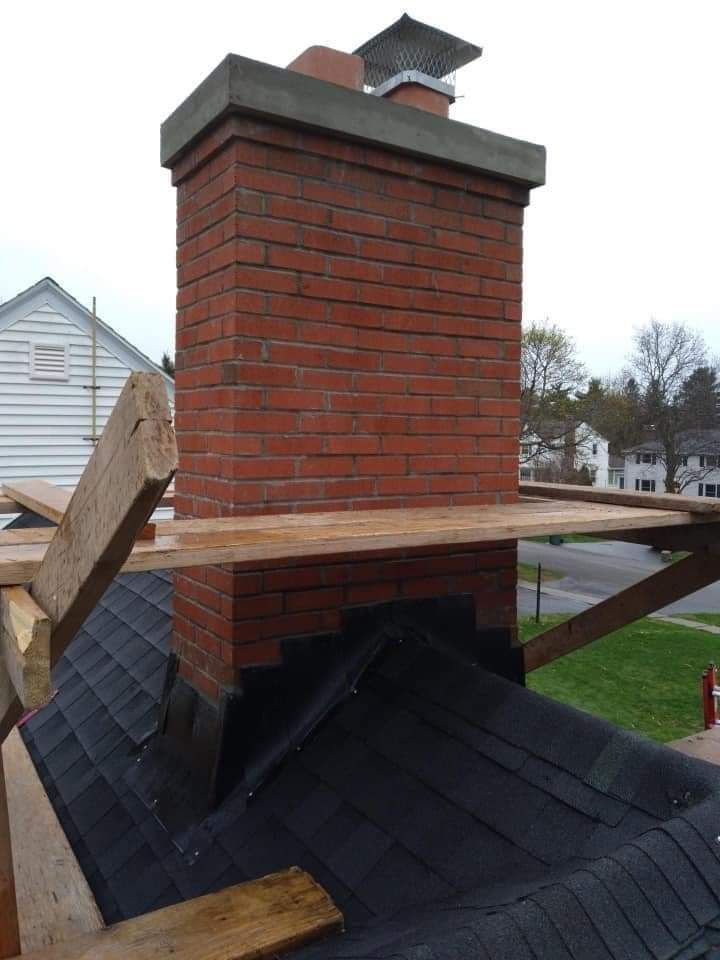 A brick chimney is sitting on top of a black roof.