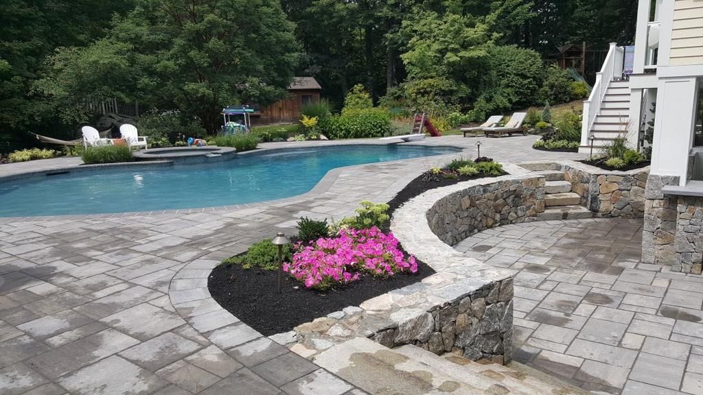 A large swimming pool is surrounded by a patio and flowers.