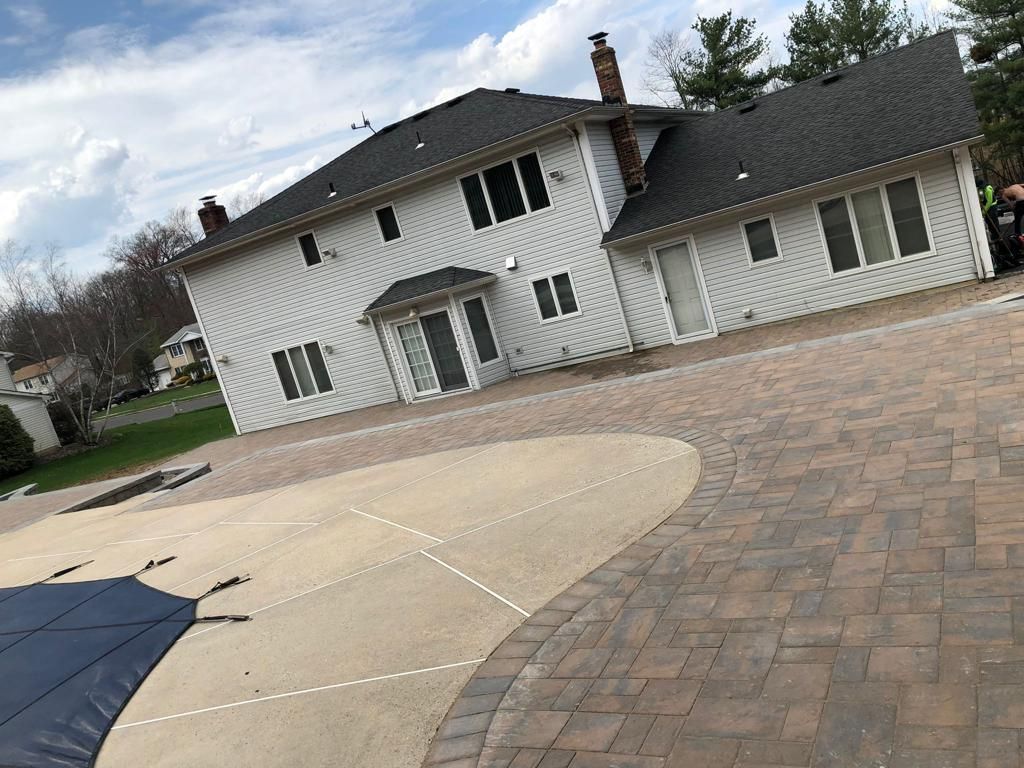 Two-story white house with a brick paved driveway and a covered pool on a cloudy day.