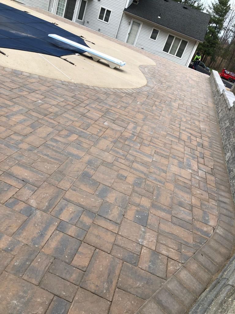 Brick paver patio with a pool cover in front of a white house.