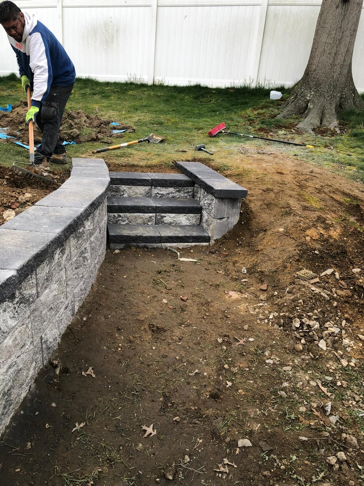 A man is digging in the dirt next to a wall and stairs.
