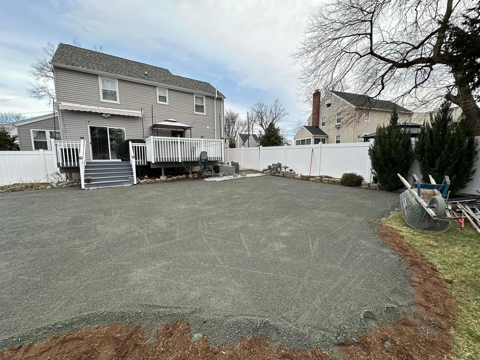 The backyard of a house with a gravel driveway and a white fence.
